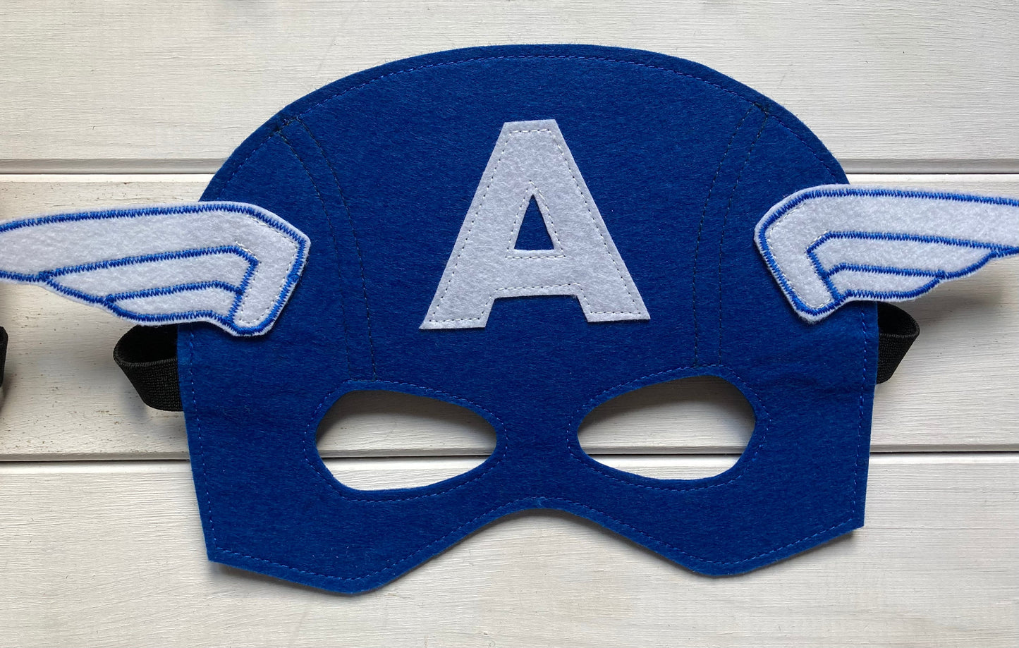 captain america Blue superhero mask with 'A' and wings on a wooden surface