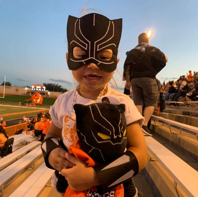 a young kid wearing handmade felt black panther mask and cuffs & looks comfortable and happy