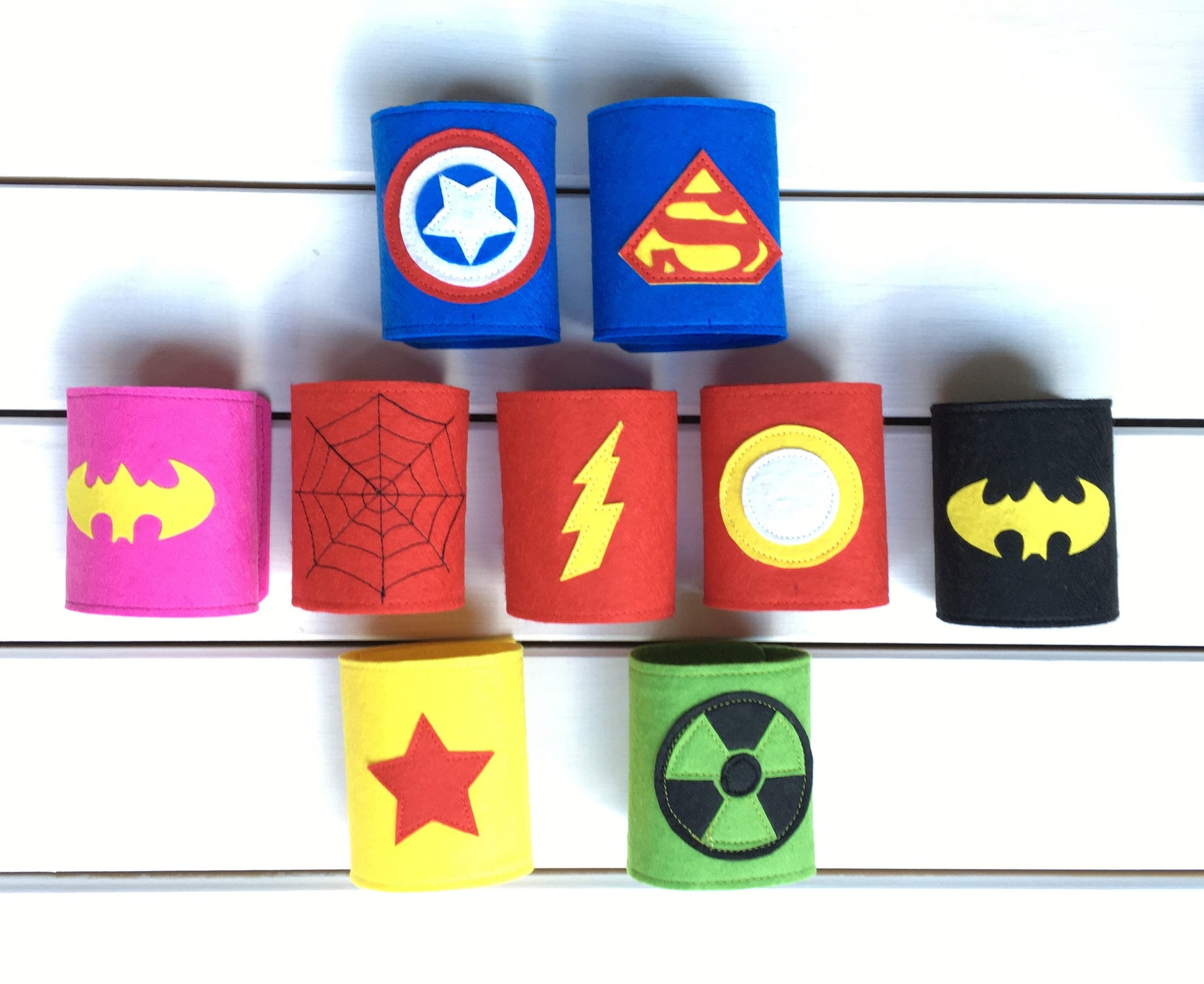 Superhero-themed wristbands with various symbols on a white wooden background 