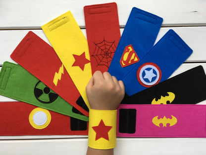 Superhero-themed wristbands with various symbols on a white wooden background 