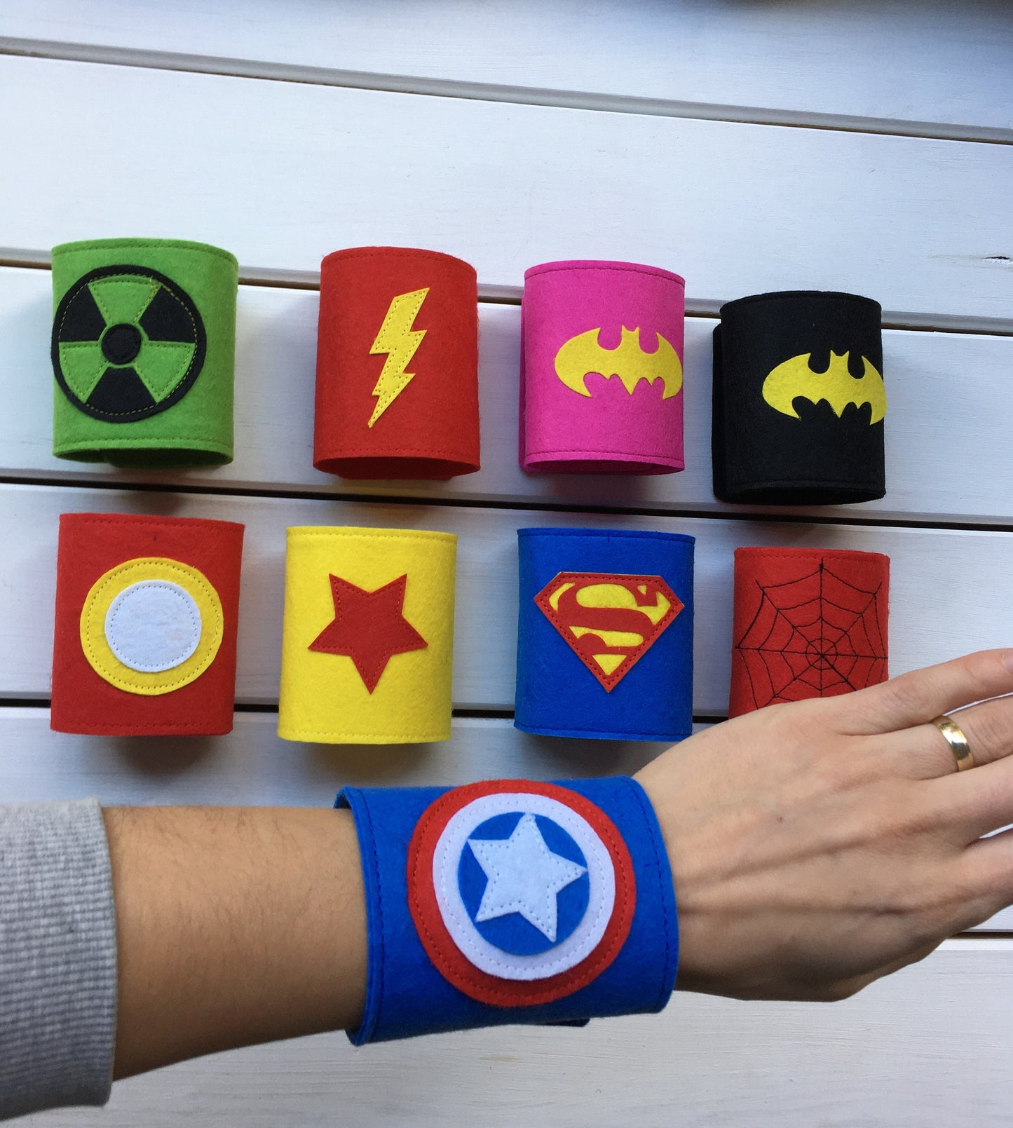 Superhero-themed wristbands with various symbols on a white wooden background 