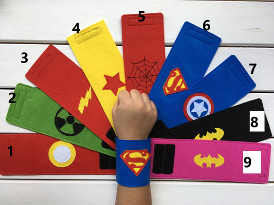 nine types of Superhero-themed wristbands with various symbols on a white wooden background 