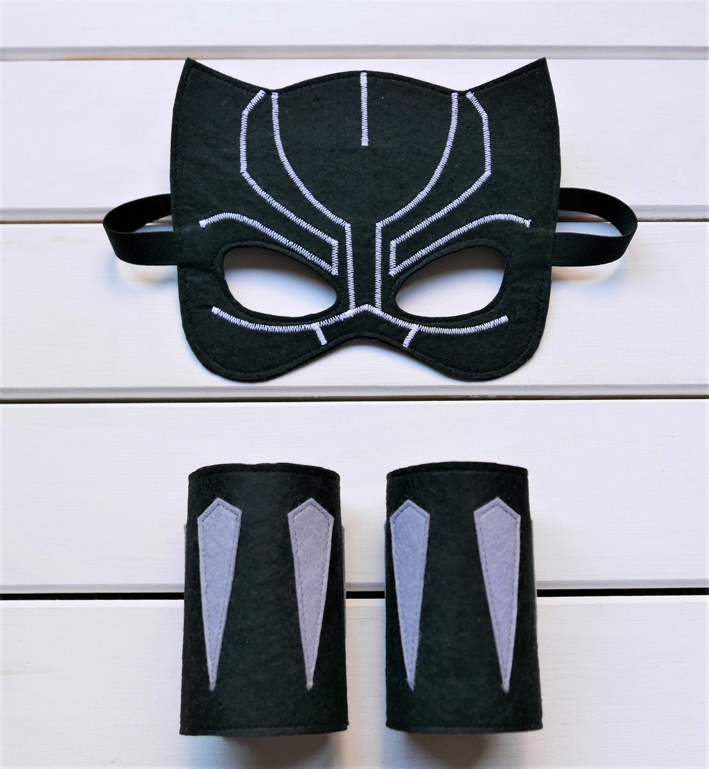 Handmade felt Black Panther mask and arm cuffs presented on a white wooden surface
