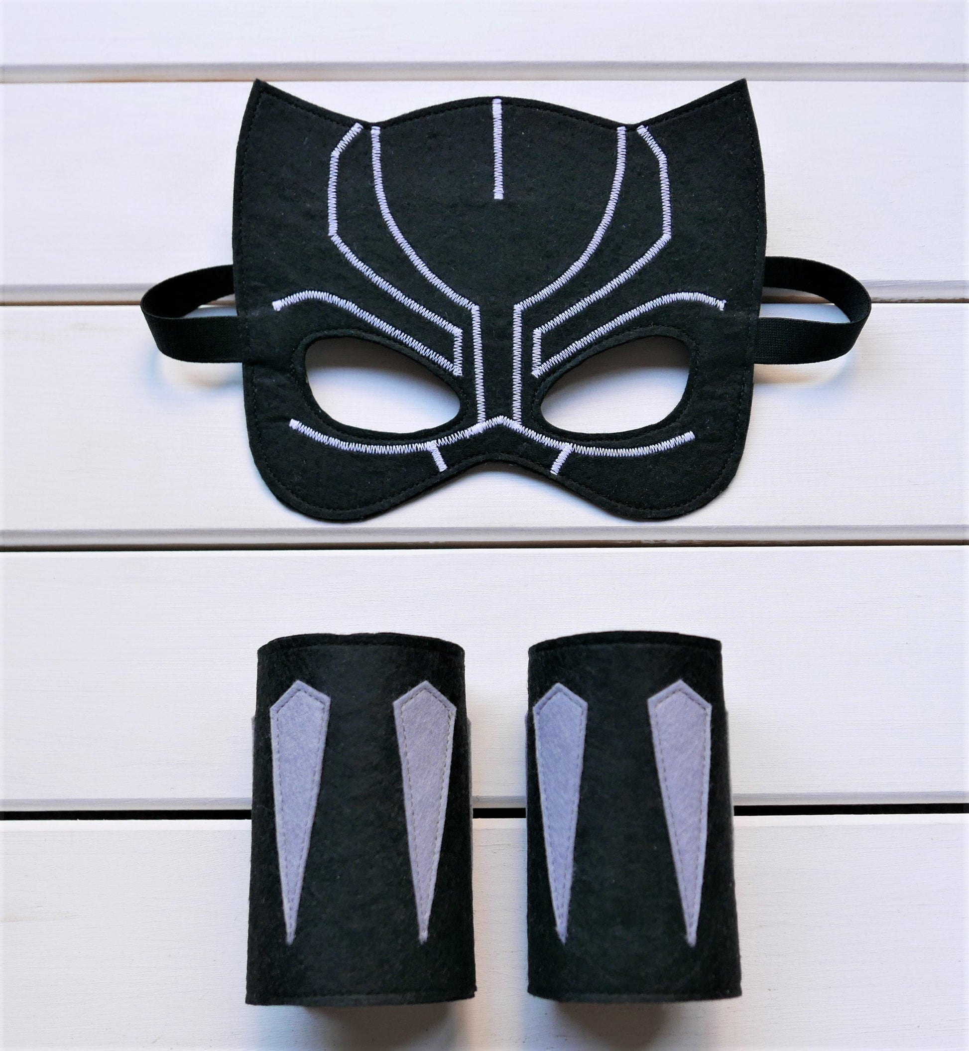 Handmade felt Black Panther mask and arm cuffs presented on a white wooden surface