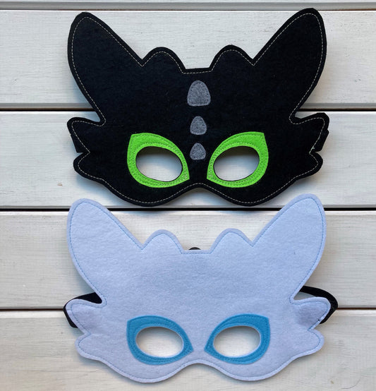 Two handmade felt dragon masks, one black with green eyes and one blue with white eyes, resembles from dragons of how to train your dragon.