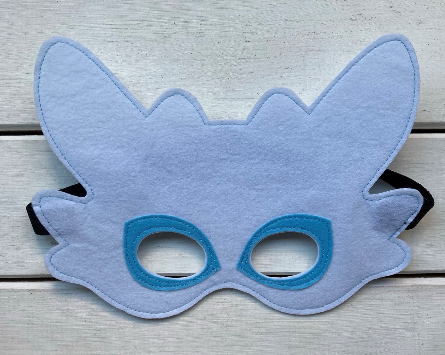 Two handmade felt dragon masks, one black with green eyes and one blue with white eyes, resembles from dragons of how to train your dragon.
