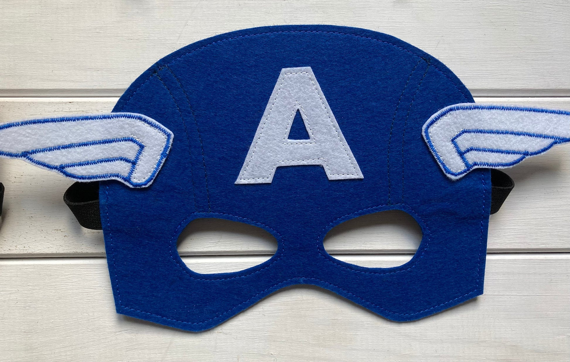 captain america Blue superhero mask with 'A' and wings on a wooden surface
