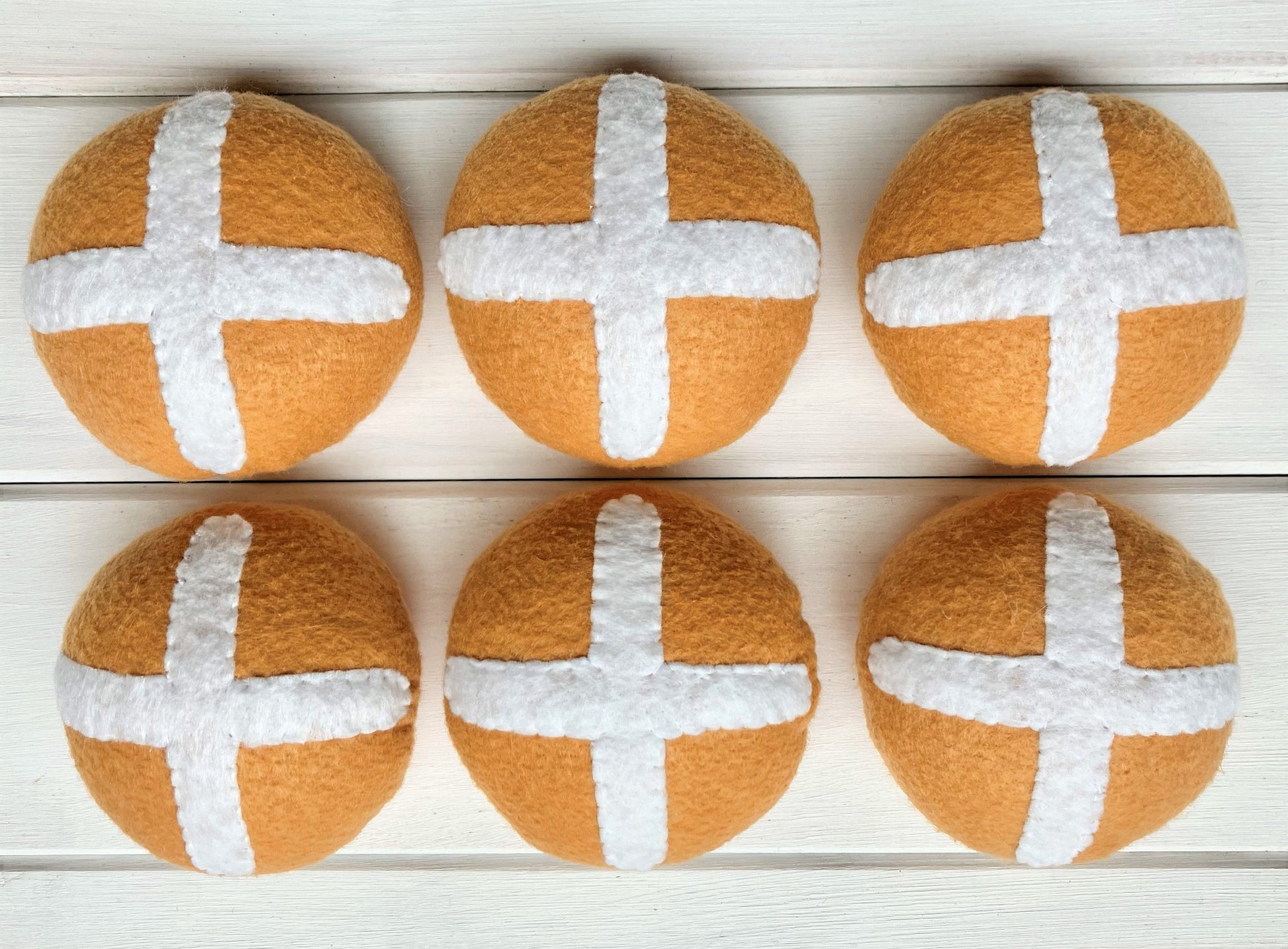 Six round bread rolls with white crosses, hot cross buns,  presented on a wooden surface