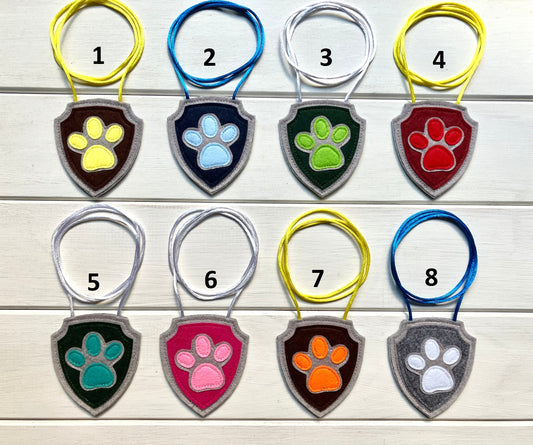 eight handmade felt badges with hanging strings in various colors each representing a paw patrol character