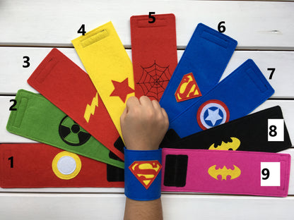 Nine felt wristbands with different superhero logos, including Superman, Batman, Spiderman, and Captain America. The wristbands are red, yellow, green, blue, black, and pink.